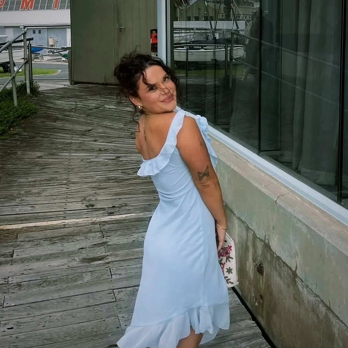 Woman in pale-blue dress at a marina, tanned back and arms