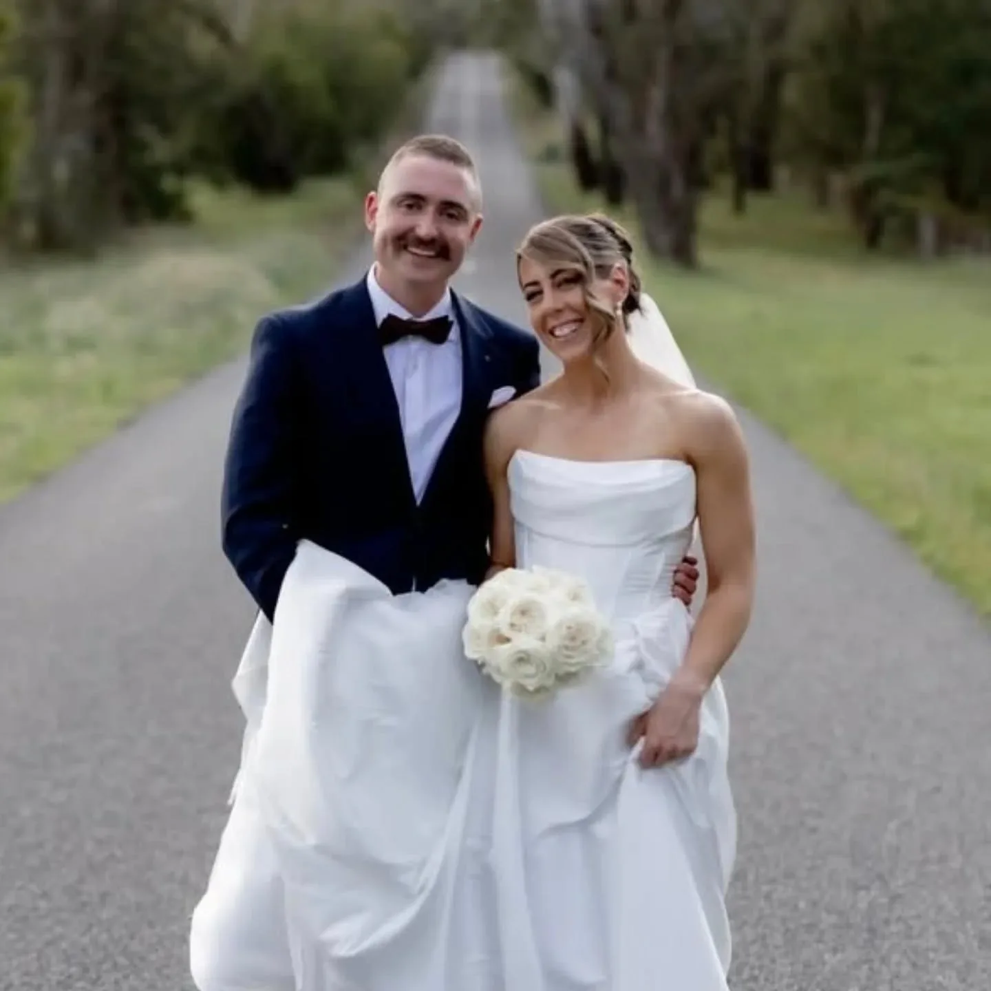 Bronzed bride and groom on a tree-lined road