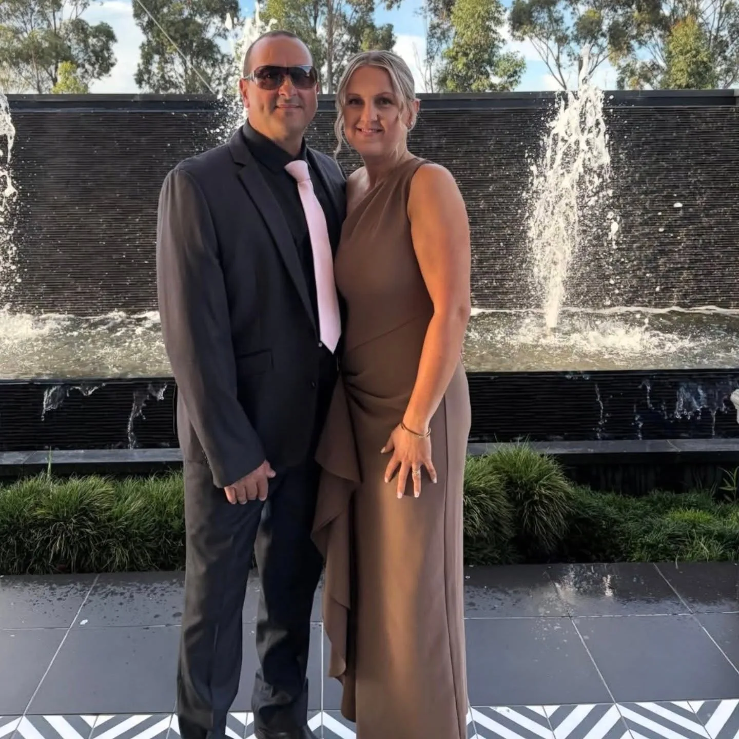 Couple by a fountain, tanned woman in a caramel gown