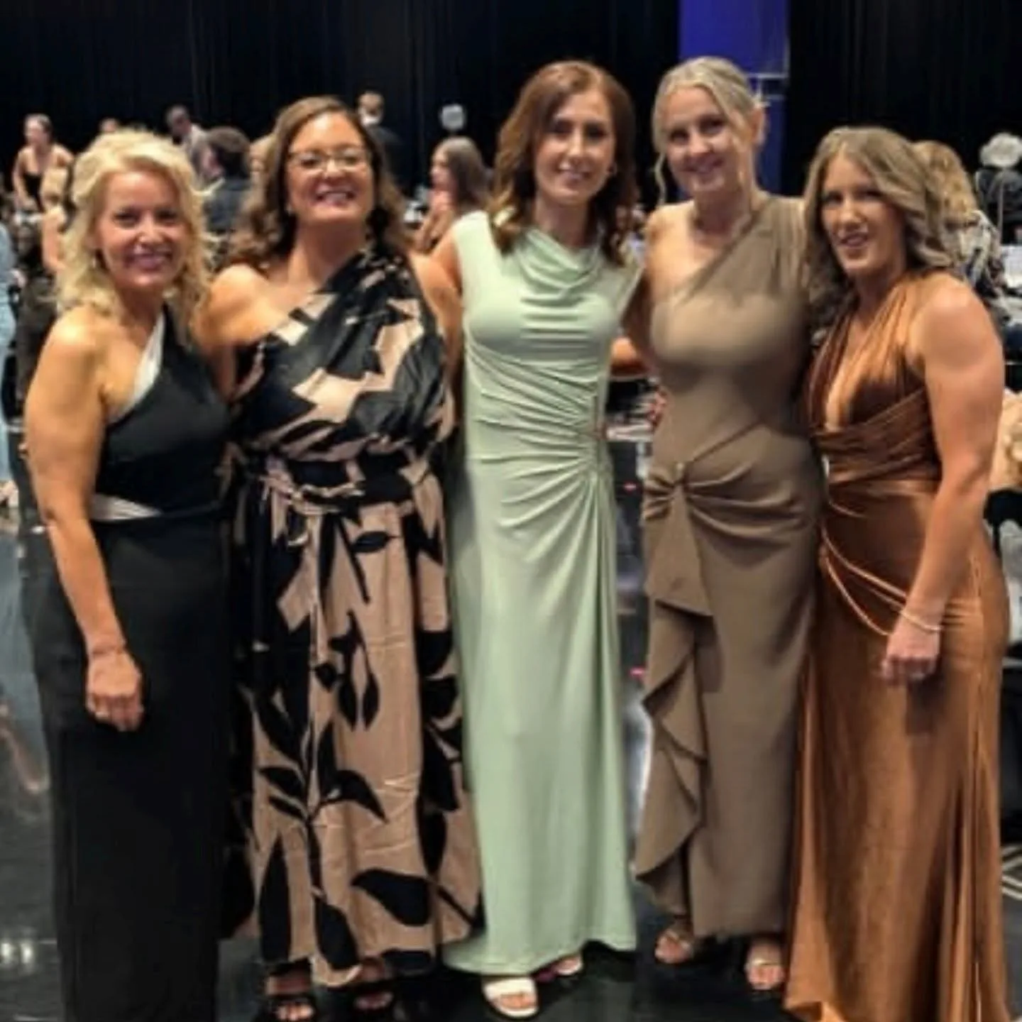 Five women in evening gowns at a gala, warm tans